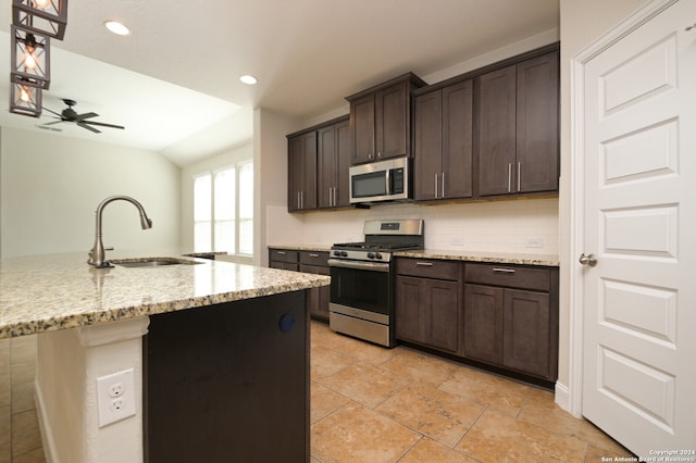 kitchen with appliances with stainless steel finishes, dark brown cabinets, light stone countertops, sink, and a kitchen island with sink