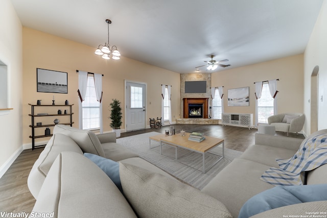 living room with ceiling fan with notable chandelier, hardwood / wood-style floors, and a stone fireplace