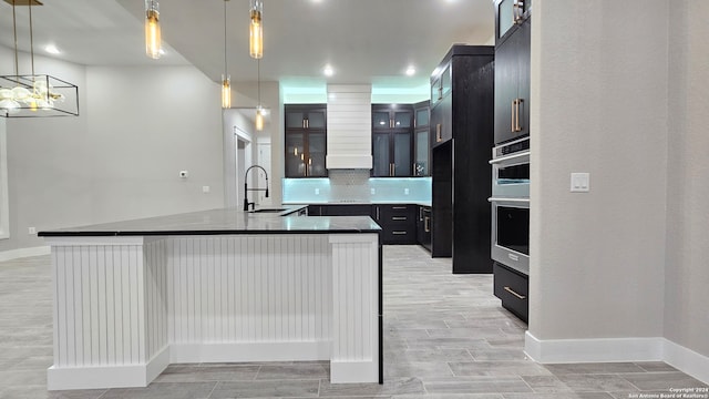 kitchen featuring light wood-type flooring, decorative light fixtures, a kitchen island with sink, and sink