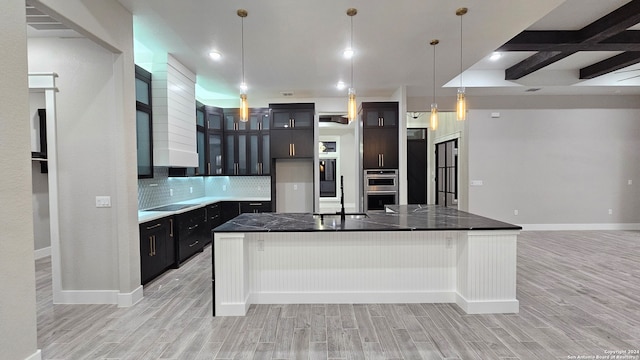 kitchen with stainless steel double oven, backsplash, light hardwood / wood-style floors, a breakfast bar, and a center island with sink