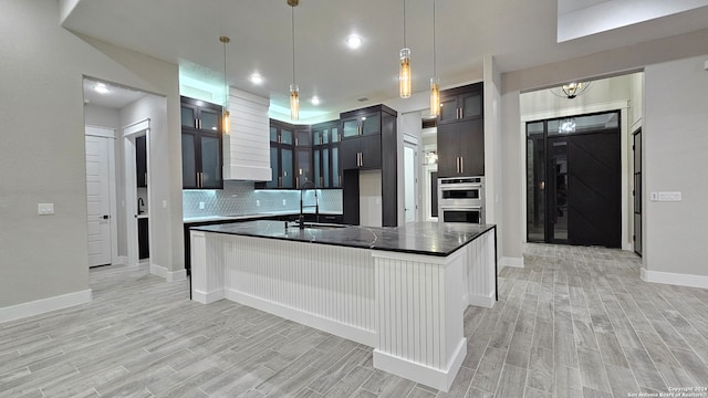 kitchen featuring backsplash, sink, light hardwood / wood-style flooring, an island with sink, and double oven