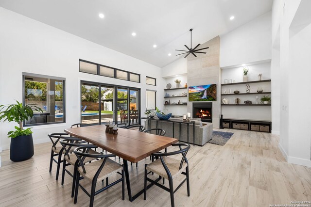 dining room featuring high vaulted ceiling, a tiled fireplace, ceiling fan, and light wood-type flooring