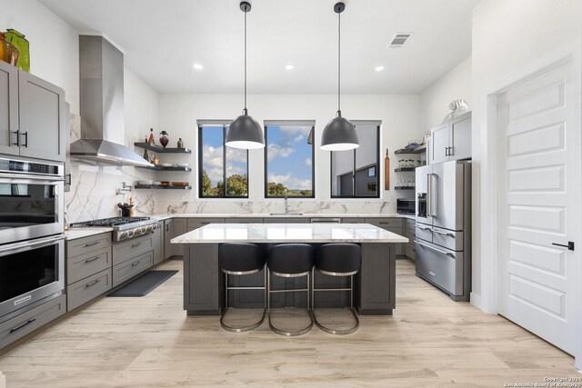 kitchen with a kitchen bar, wall chimney exhaust hood, a kitchen island, light wood-type flooring, and appliances with stainless steel finishes