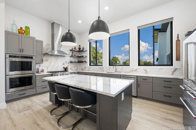 kitchen with appliances with stainless steel finishes, a breakfast bar area, decorative light fixtures, a kitchen island, and wall chimney range hood