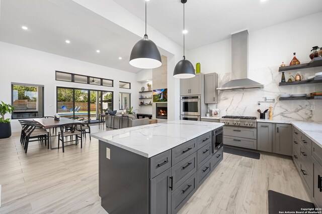 kitchen with stainless steel appliances, a kitchen island, wall chimney range hood, gray cabinets, and pendant lighting