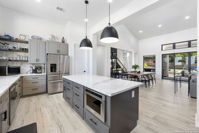 kitchen with pendant lighting, stainless steel appliances, a kitchen island, and light stone countertops