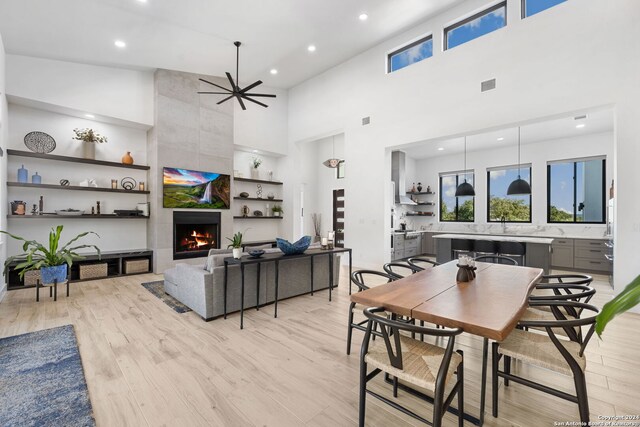 dining space with high vaulted ceiling, a tile fireplace, ceiling fan, and light hardwood / wood-style flooring