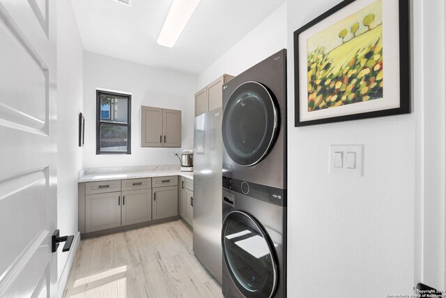 clothes washing area featuring cabinets, stacked washer / dryer, and light hardwood / wood-style flooring