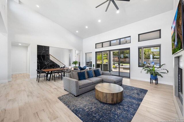 living room featuring a fireplace, a high ceiling, ceiling fan, and light hardwood / wood-style flooring