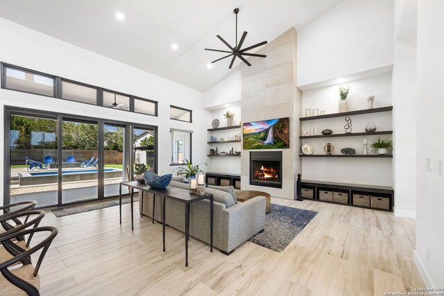 living room with high vaulted ceiling, a tiled fireplace, ceiling fan, and light wood-type flooring