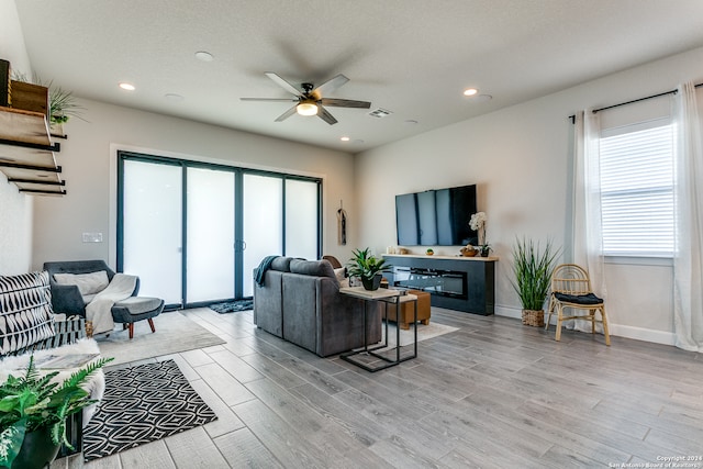 living room with a textured ceiling, ceiling fan, and light hardwood / wood-style flooring