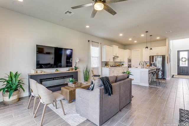 living room with ceiling fan, sink, and light wood-type flooring