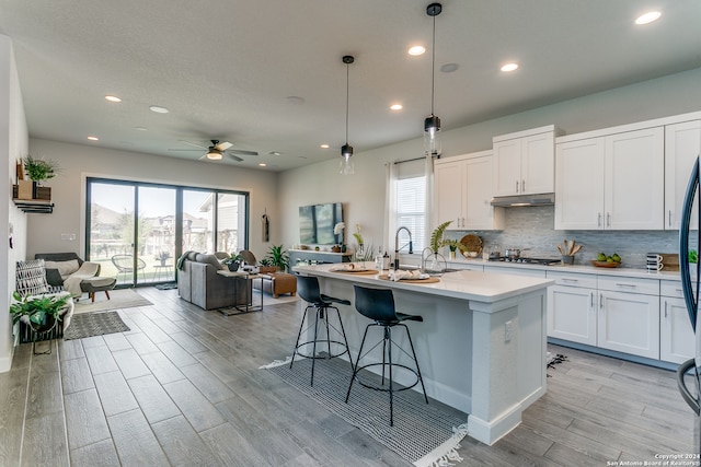 kitchen with a wealth of natural light, decorative light fixtures, an island with sink, and white cabinets