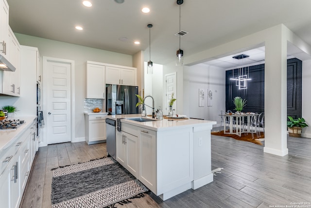 kitchen with white cabinets, light hardwood / wood-style floors, hanging light fixtures, and an island with sink