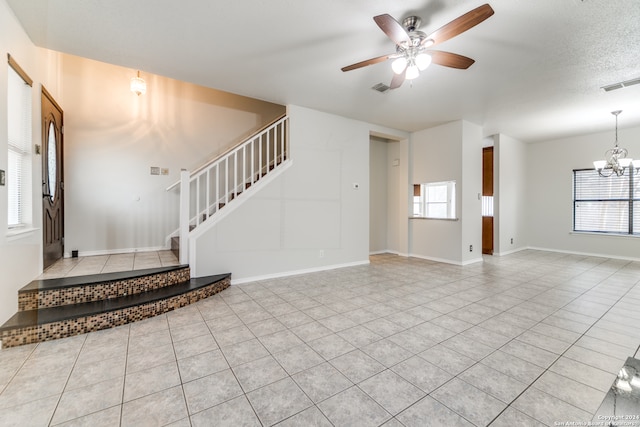 unfurnished living room with a textured ceiling, ceiling fan with notable chandelier, and light tile patterned flooring