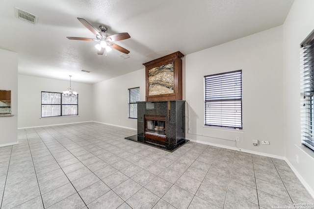 unfurnished living room featuring a textured ceiling, light tile patterned floors, a premium fireplace, and ceiling fan with notable chandelier