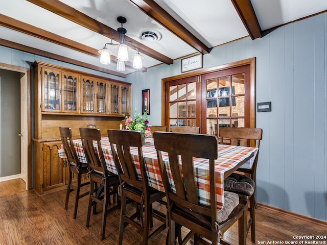 dining area featuring dark wood-type flooring, wood walls, beamed ceiling, and an inviting chandelier