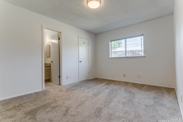 unfurnished bedroom with a textured ceiling, light carpet, and connected bathroom