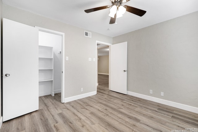 unfurnished bedroom featuring ceiling fan, a closet, light hardwood / wood-style flooring, and a walk in closet