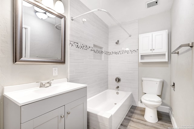 full bathroom with tiled shower / bath combo, vanity, hardwood / wood-style flooring, and toilet