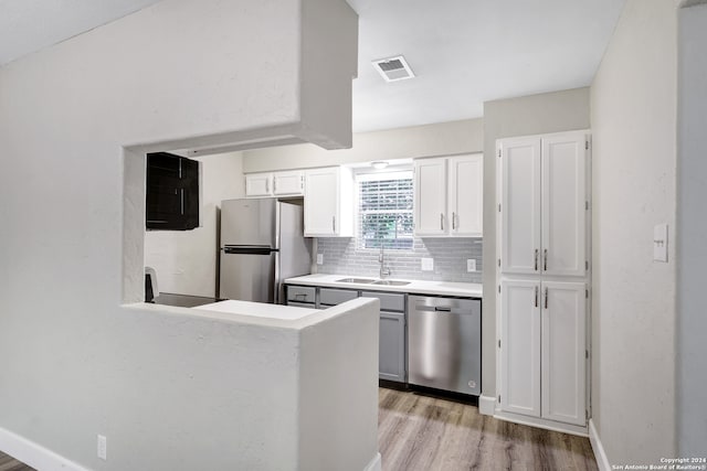 kitchen featuring tasteful backsplash, stainless steel appliances, sink, light hardwood / wood-style floors, and white cabinets