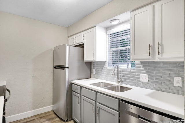 kitchen with stainless steel appliances, sink, tasteful backsplash, light hardwood / wood-style flooring, and white cabinets