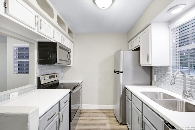 kitchen featuring sink, tasteful backsplash, white cabinetry, light wood-type flooring, and appliances with stainless steel finishes