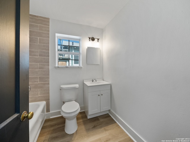 bathroom featuring toilet, vanity, wood-type flooring, and a tub