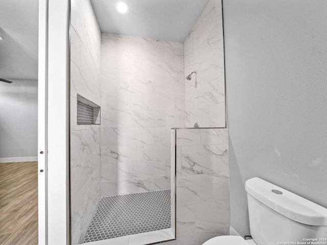 bathroom with toilet, hardwood / wood-style flooring, and tiled shower