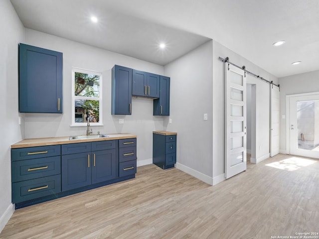 kitchen featuring butcher block counters, sink, blue cabinetry, light hardwood / wood-style flooring, and a barn door