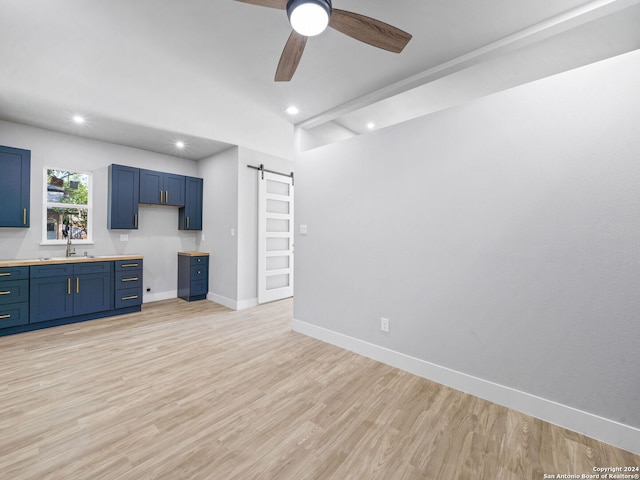 kitchen with sink, ceiling fan, blue cabinetry, a barn door, and light wood-type flooring