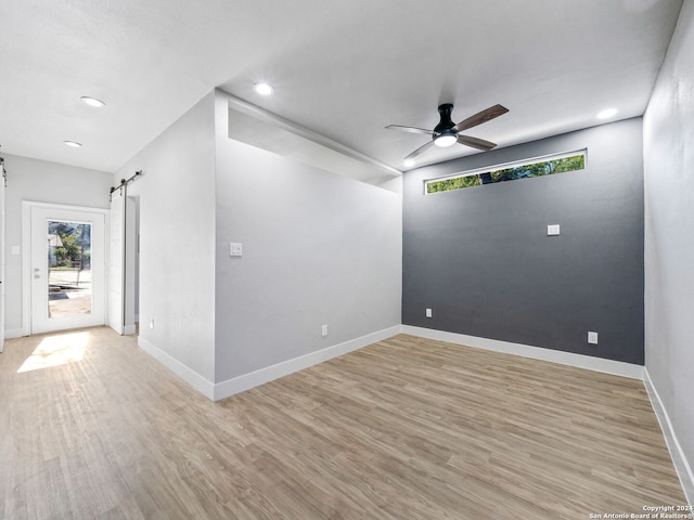 empty room with light hardwood / wood-style flooring, a barn door, and ceiling fan