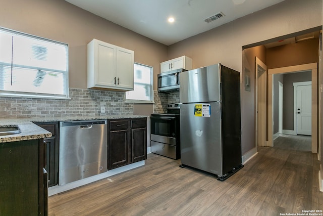 kitchen featuring white cabinetry, appliances with stainless steel finishes, light stone countertops, backsplash, and wood-type flooring