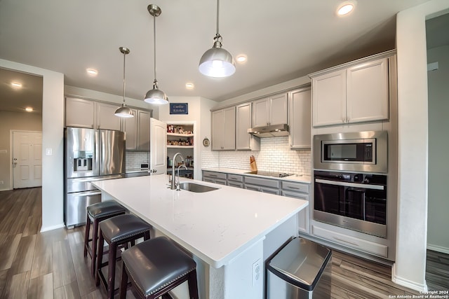 kitchen featuring hanging light fixtures, gray cabinetry, an island with sink, and appliances with stainless steel finishes