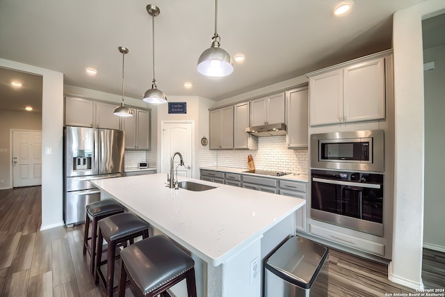 kitchen featuring stainless steel appliances, dark hardwood / wood-style flooring, sink, an island with sink, and pendant lighting