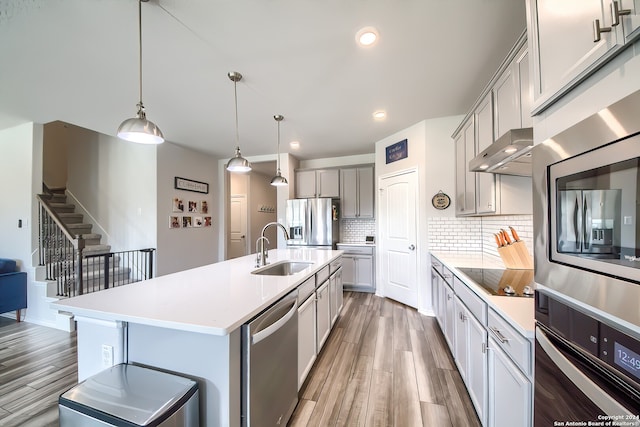 kitchen featuring wood-type flooring, hanging light fixtures, sink, an island with sink, and appliances with stainless steel finishes