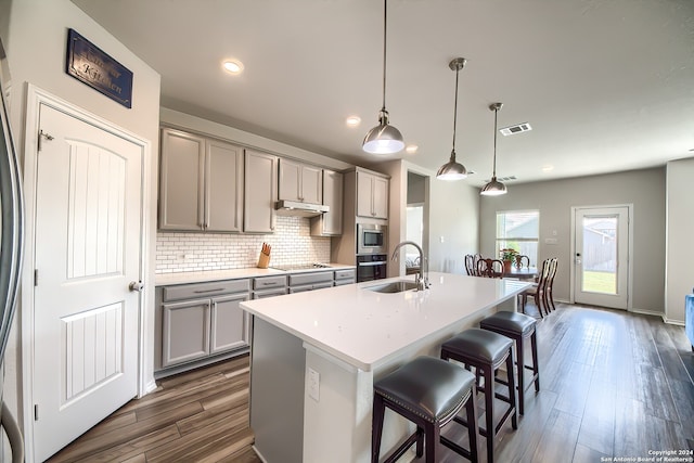 kitchen featuring gray cabinetry, a center island with sink, appliances with stainless steel finishes, decorative light fixtures, and dark hardwood / wood-style floors