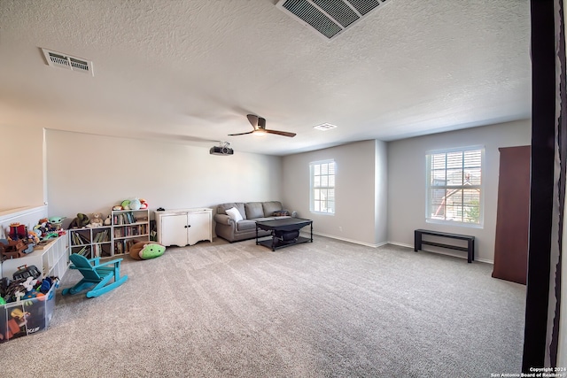 playroom with ceiling fan, a textured ceiling, and light carpet