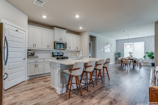 kitchen featuring white cabinetry, decorative light fixtures, an island with sink, and stainless steel appliances