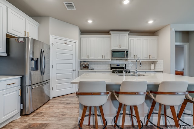 kitchen with white cabinets, a center island with sink, light wood-type flooring, and appliances with stainless steel finishes