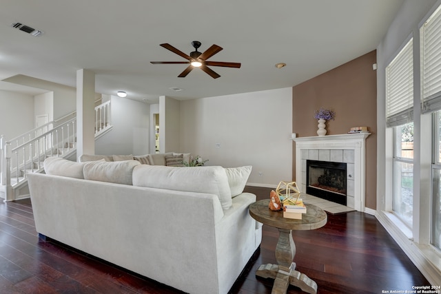 living room with a tiled fireplace, dark wood-type flooring, and ceiling fan