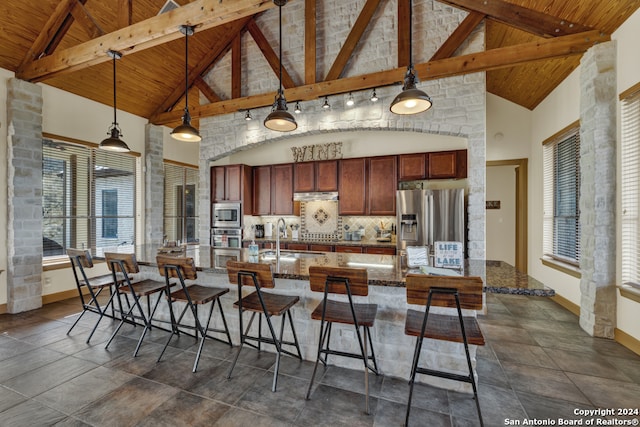 kitchen featuring appliances with stainless steel finishes, high vaulted ceiling, hanging light fixtures, an island with sink, and a breakfast bar