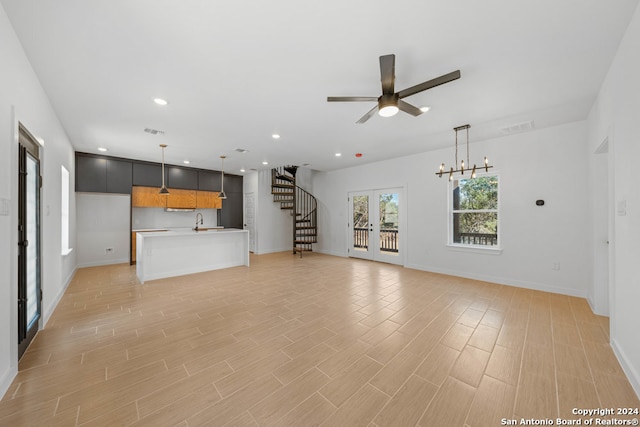 unfurnished living room with french doors, light wood-type flooring, and ceiling fan with notable chandelier