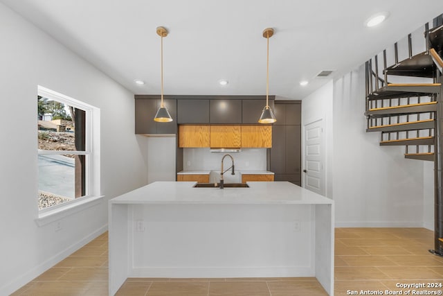 kitchen featuring an island with sink, extractor fan, sink, and pendant lighting