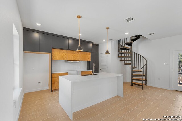 kitchen with hanging light fixtures, an island with sink, light hardwood / wood-style flooring, and exhaust hood