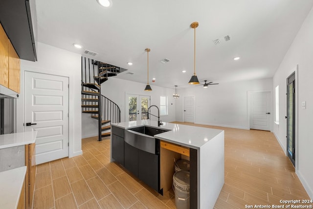 kitchen featuring sink, ceiling fan, decorative light fixtures, an island with sink, and light hardwood / wood-style flooring