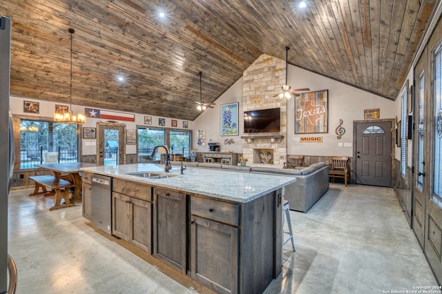 kitchen with sink, hanging light fixtures, light stone countertops, an island with sink, and stainless steel dishwasher