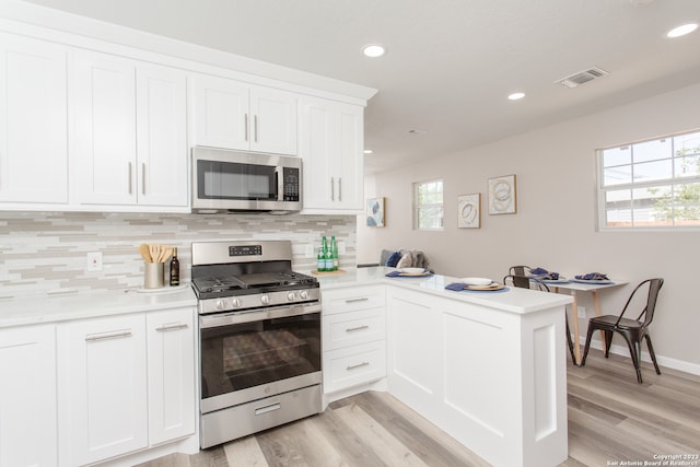 kitchen featuring stainless steel appliances, white cabinets, light wood-type flooring, and kitchen peninsula