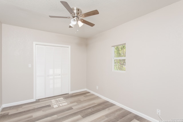 empty room with a textured ceiling, light wood-type flooring, and ceiling fan