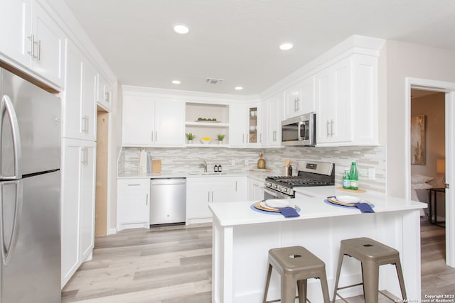 kitchen featuring stainless steel appliances, light hardwood / wood-style floors, white cabinetry, tasteful backsplash, and a kitchen bar